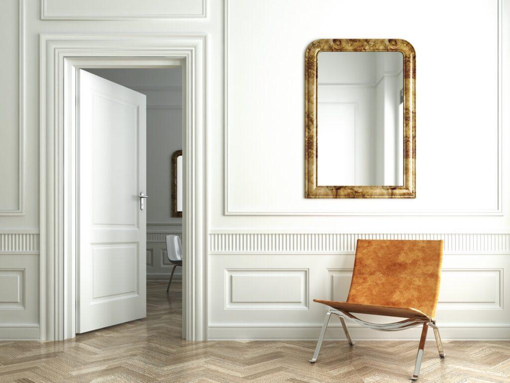 classic white interior door opening into a bedroom with gold mirror and burnt sienna sitting chair